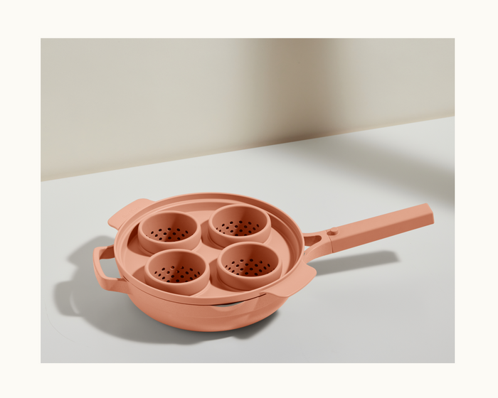 A peach-colored Egg Poacher pan with a handle and four round silicone egg cups is displayed on a white surface.
