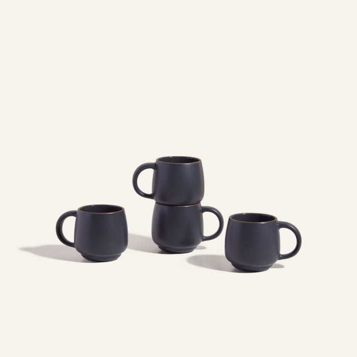 Two Night + Day Mugs are stacked atop each other, while two more matte black ceramic stoneware mugs stand beside them, highlighting their generous capacity against a plain light background.