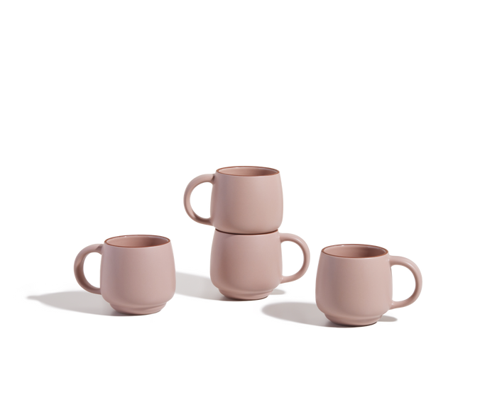 Four Night + Day Mugs in pink ceramic stoneware—two upright, two stacked—are displayed on a white background. These stackable mugs offer ample capacity for enjoying your favorite drinks.