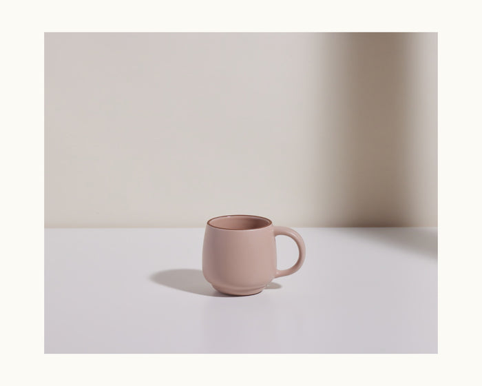 A Night + Day Mug in plain mauve ceramic stoneware sits on a white surface against a light, neutral background, with a soft shadow cast to the left.