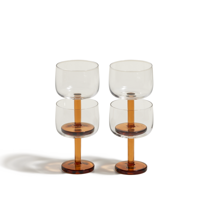 The Party Coupes set includes four modern wine glasses with clear bowls and amber stems and bases, arranged in two vertical stacks on a white background—ideal party glassware for any occasion.