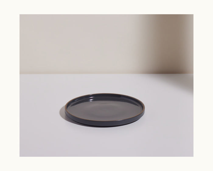 A hand-glazed dark gray ceramic Salad Plate rests on a white surface with a light background, bringing elegance to any tableware collection.