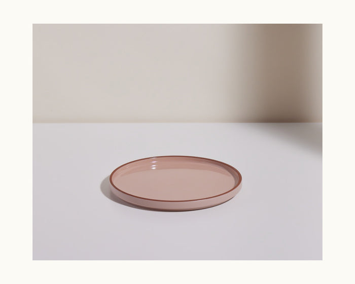 A round, shallow, light pink Salad Plate sits on a white surface with a pale background, displaying elegant hand-glazed ceramic plates ideal for stylish tableware settings.
