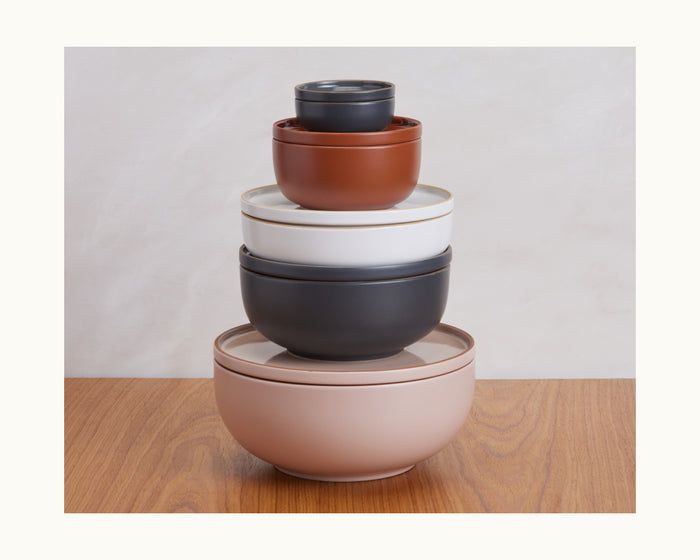 A set of five Serving Bowls in assorted sizes is stacked on a wooden surface against a light background, highlighting the stylish and space-saving design of these vibrant, stackable ceramic tableware pieces.