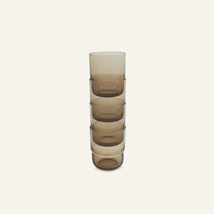 A stack of five Short Night + Day Glasses made from brown-tinted recycled glass is neatly arranged against a plain light background, highlighting their modern, versatile design.